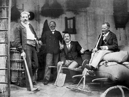 Michel, son frère Étienne, un inconnu et l’oncle Auguste Gourdin posent sous la remise, des outils à la main. De gauche à droite : une petite houe à long manche, une binette, une houe pleine et un râteau à fenaison. ©Archives de la famille Savard